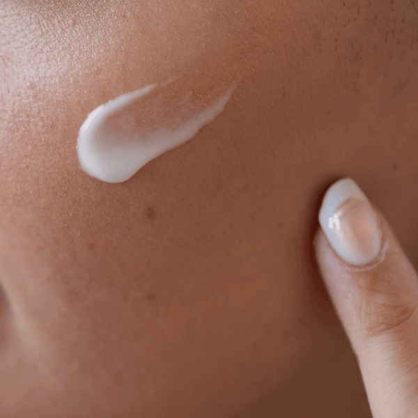 Close-up of a hand applying white cream to skin