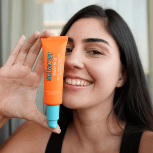 Woman holding an orange skincare product with 'Skinvest' branding.

