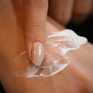 Hand applying a white cream or lotion to skin