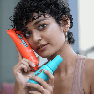 Woman holding two colorful hair care products with a blurred background