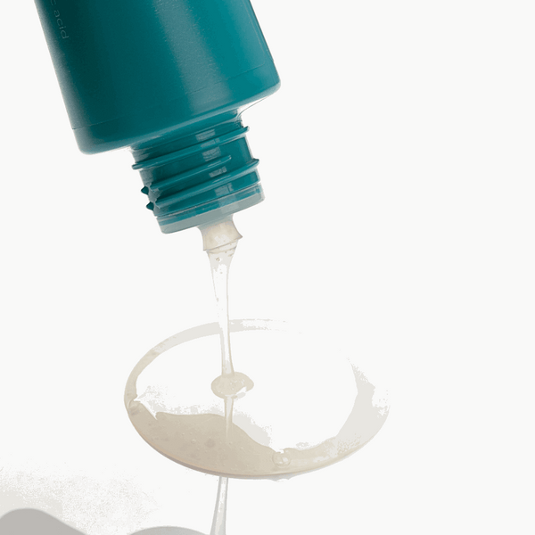 Close-up of a teal bottle with a pump dispensing a clear liquid onto a white surface.