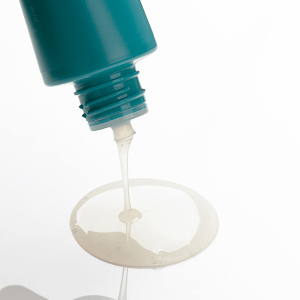 Close-up of a teal bottle with a pump dispensing a clear liquid onto a white surface.