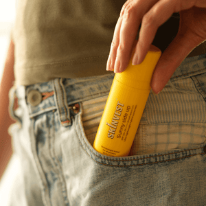 Person holding a yellow bottle of Sunscreen in their pocket