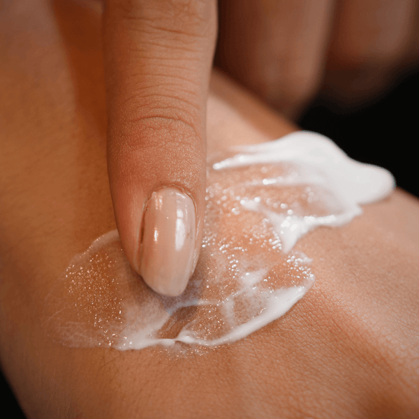 Hand applying a white cream or lotion to skin