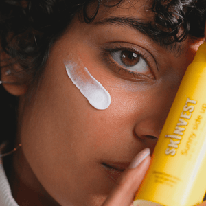 Person applying sunscreen to their face with a Skinvest bottle.